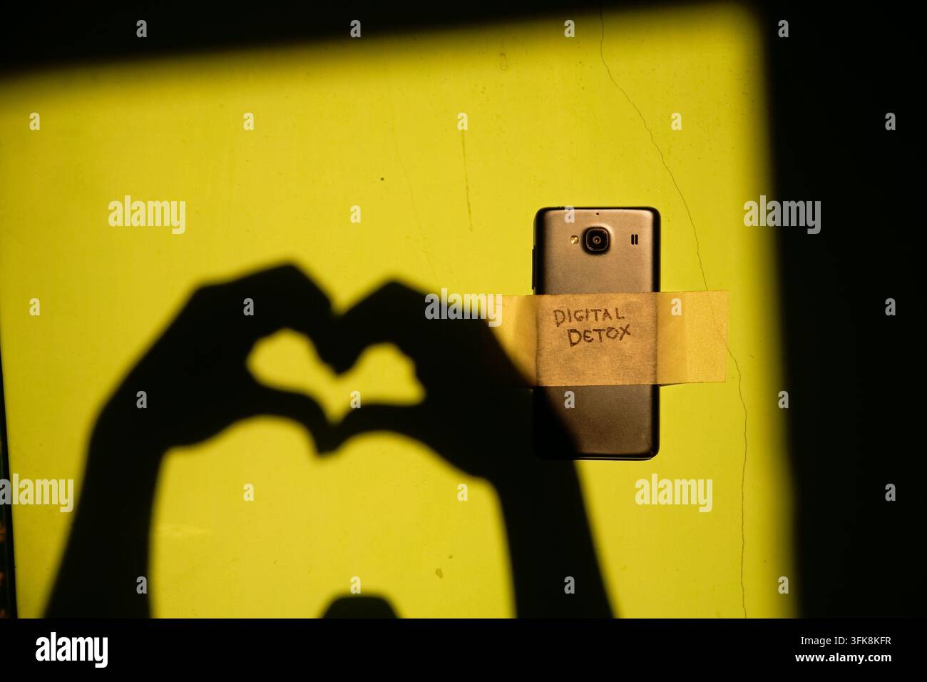 Nahaufnahme eines Smartphones, das mit dem Textwort „digitaler Entzug“ beschriftet ist und mit dem Schatten einer Liebessymbol-Geste der Hand auf der schmutzigen Wand Stockfoto