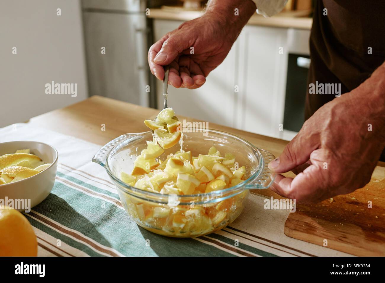 Senior-Mann mischt geschnittene Zitrusfrüchte in einer Glasschale Stockfoto