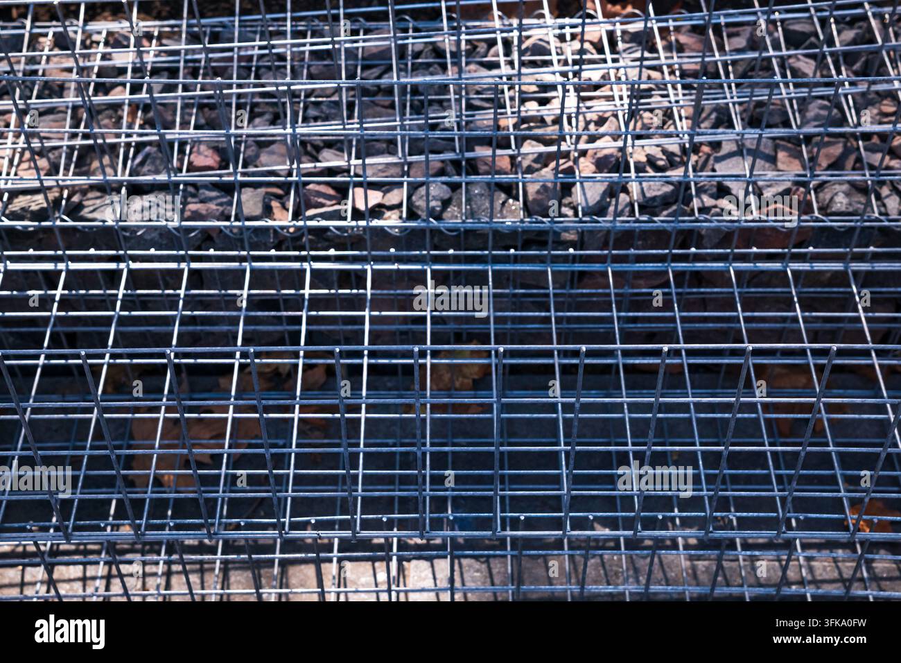 Abstrakte Nahaufnahme, Ansicht von oben, von galvanisiertem Stahldrahtgeflecht, das über Schotter im Freien auf einer Baustelle gestapelt ist. Stockfoto