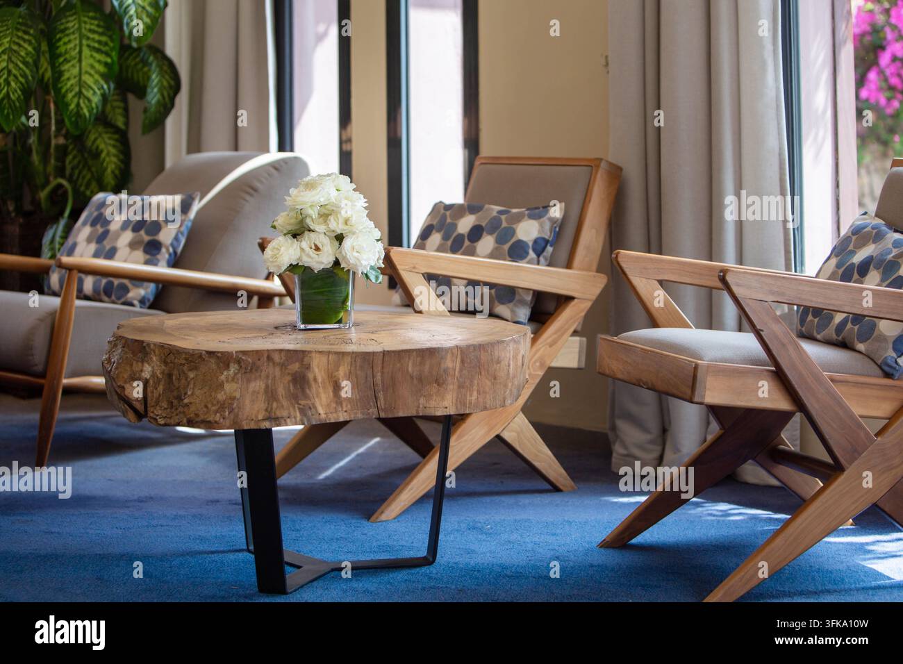 Wohnzimmer-Sitzbereich mit Blumenarrangement. Modernes, gemütliches Hotel-Lounge-Interieur mit Holzkaffeetisch, bequemen Sesseln und frischen weißen Blumen Stockfoto