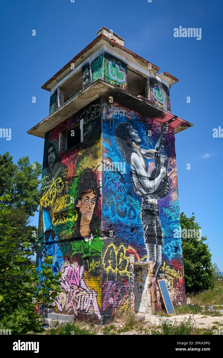 Altess industrielles oder militärisches Turmgebäude, das stark mit farbenfrohem Graffiti und Street Art bedeckt ist, vor einem blauen Himmel Stockfoto