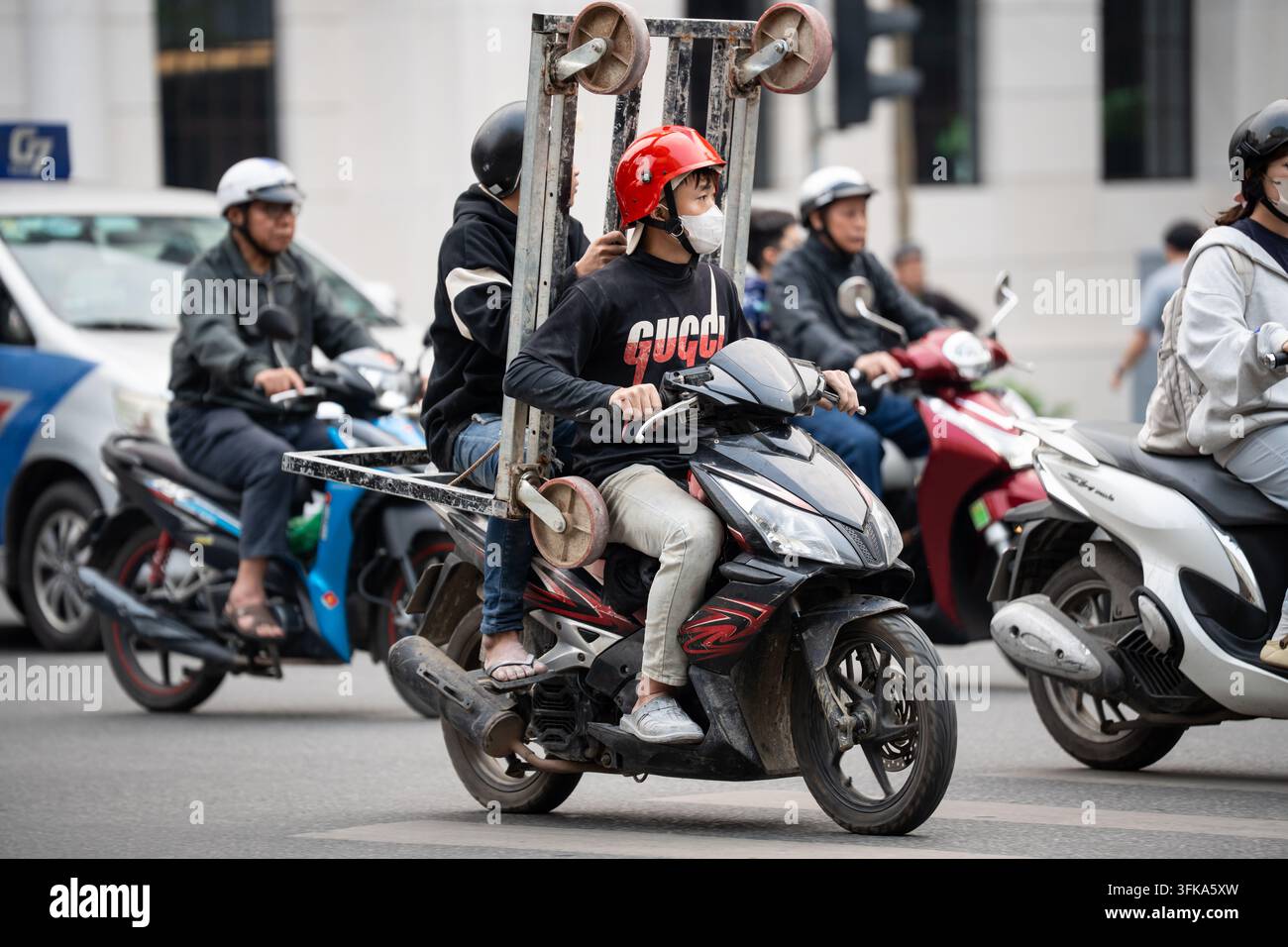 Vielbeschäftigte Hauptverkehrszeit auf der Straße in der Stadt Hanoi, Menschen auf Scootern und Motorrädern fahren durch die Fahrbahn. Stockfoto