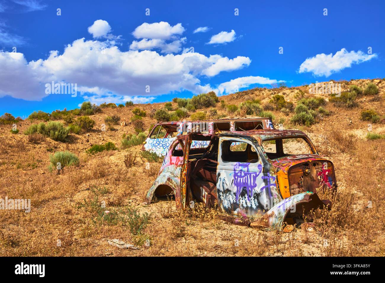 Von Graffiti bedeckte verlassene Fahrzeuge in der trockenen Wüste Nevadas fangen den Geist des Internationalen Autoforsts nahe Goldfield ein. Sonnenlicht und blauer Himmel Stockfoto