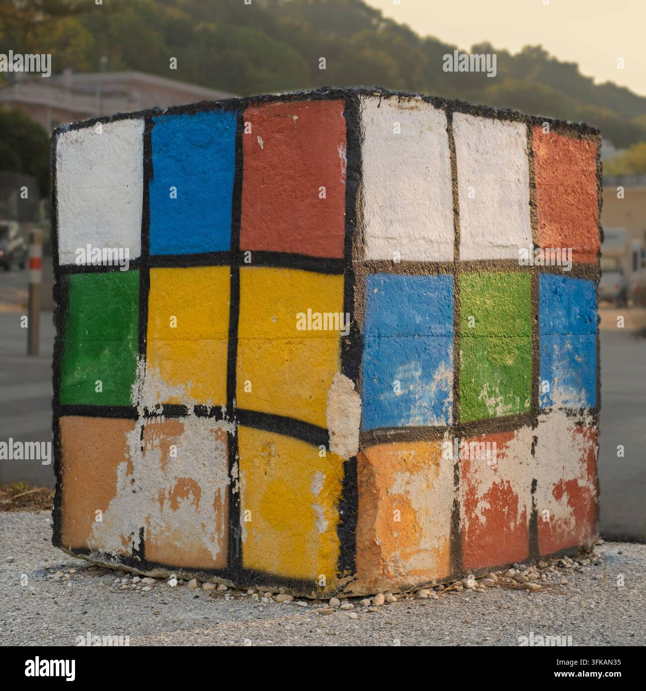 Großer Betonblock, der wie ein mehrfarbiger Rubik-Würfel bemalt ist, wird als Fahrzeugbarriere auf einem Radweg verwendet. Stockfoto