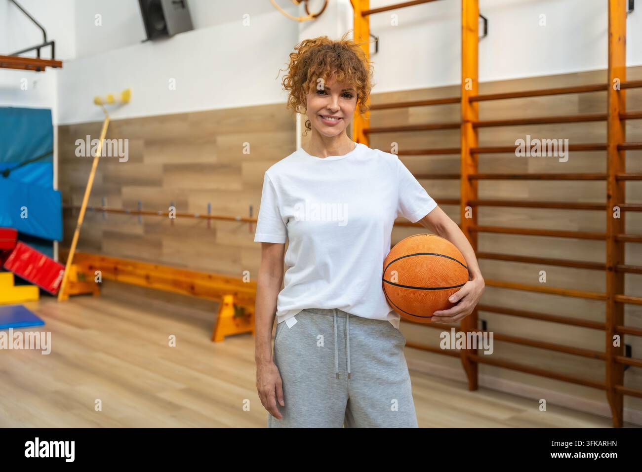 Frau lächelt und hält einen Basketball in der Schulsporthalle Stockfoto