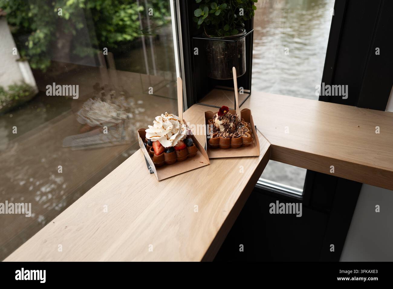 Zwei Waffel-Desserts mit Sahne und Obst darauf stehen auf einer Holztheke neben einem großen Fenster in Brügge. Stockfoto