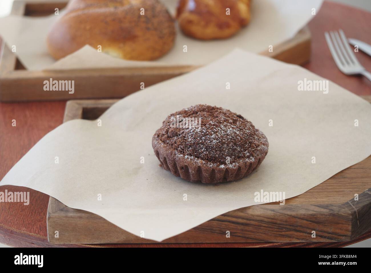 Schokoladenmuffin auf einem Holztablett mit Gebäckrollen im Hintergrund Stockfoto