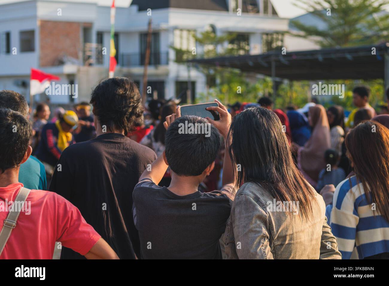Rückansicht einer vielfältigen Menschenmenge, die im Freien steht, eine kulturelle Aufführung beobachtet und mit ihren Smartphones aufnimmt. Stockfoto