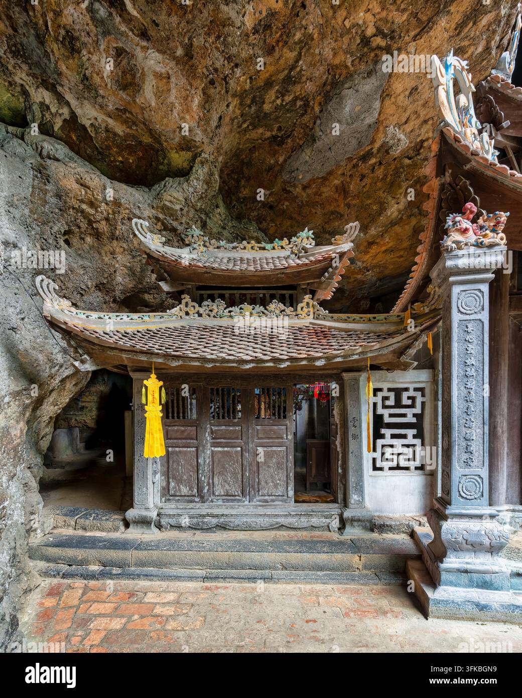 Traditioneller hölzerner Schrein, der in eine felsige Höhle der Bich-Dong-Pagode in Ninh Binh, Vietnam, eingebaut ist und kunstvolle Dachdetails und verzierte Steinmetzarbeiten aufweist Stockfoto