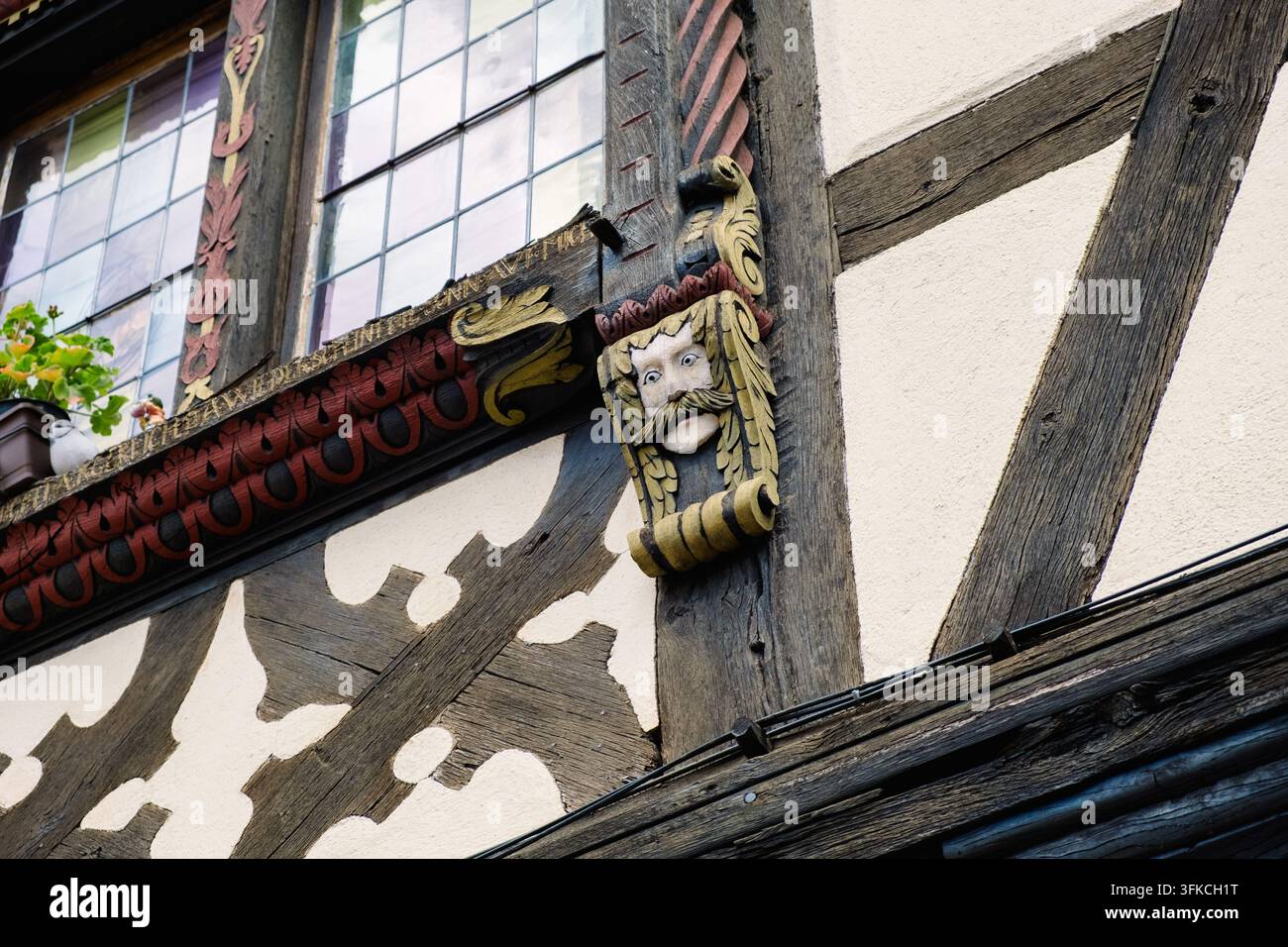 Ein geschnitztes Gesicht schmückt die Fassade eines Gebäudes in Eguisheim, Elsass, und präsentiert kunstvolle Handwerkskunst und Designelemente. Stockfoto