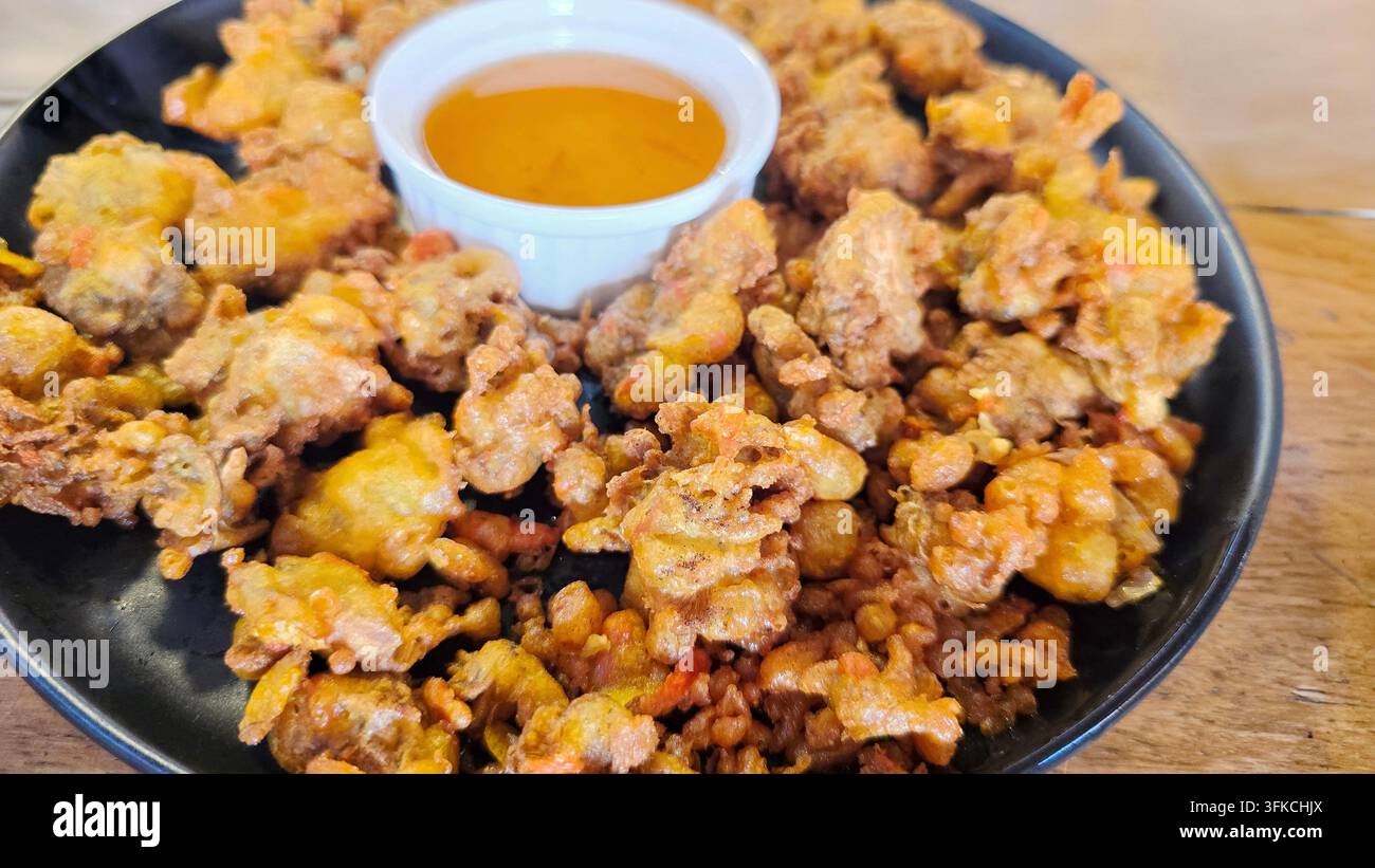 Thailändische knusprig gebratene Splitgill-Pilze serviert mit Dipping-Sauce auf einem schwarzen Teller, eine knusprige vegetarische Vorspeise. - Smartphone-aufgenommenes Stockfoto