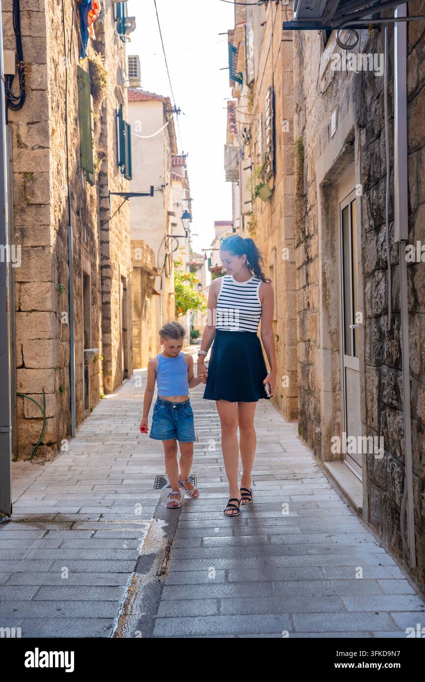 Mutter und Tochter gehen Hand in Hand durch eine enge Straße in Trogir, Kroatien. Familientravel schafft gemeinsame Erfahrungen und stärkt die Eltern-Kind-Beziehung Stockfoto