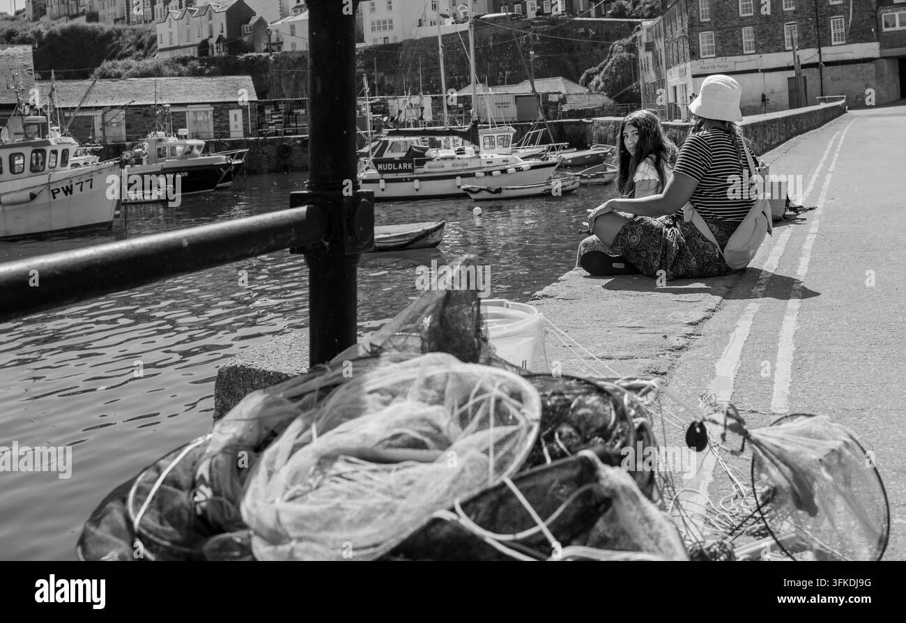 zwei Urlauber, die auf einer Hafenmauer sitzen, einer schaut in die Kamera, Mevagissy, Cornwall Stockfoto