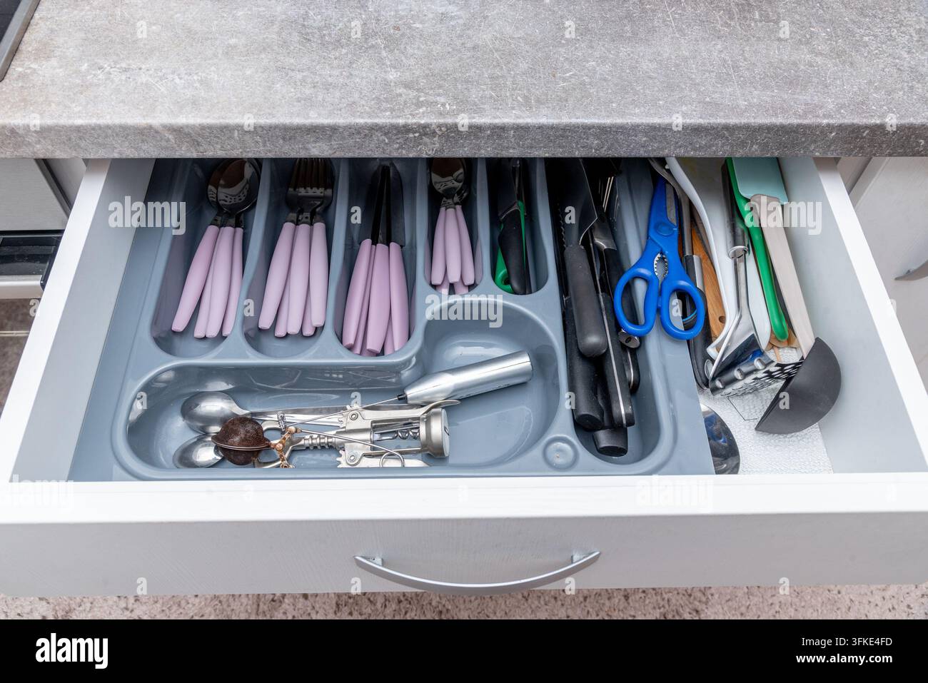 Offener Küchenschrank zeigt ordentlich angeordnetes Besteck und Kochutensilien in geformten Fächern. Organisierte Utensilien umfassen Scheren und Spezialwerkzeuge Stockfoto