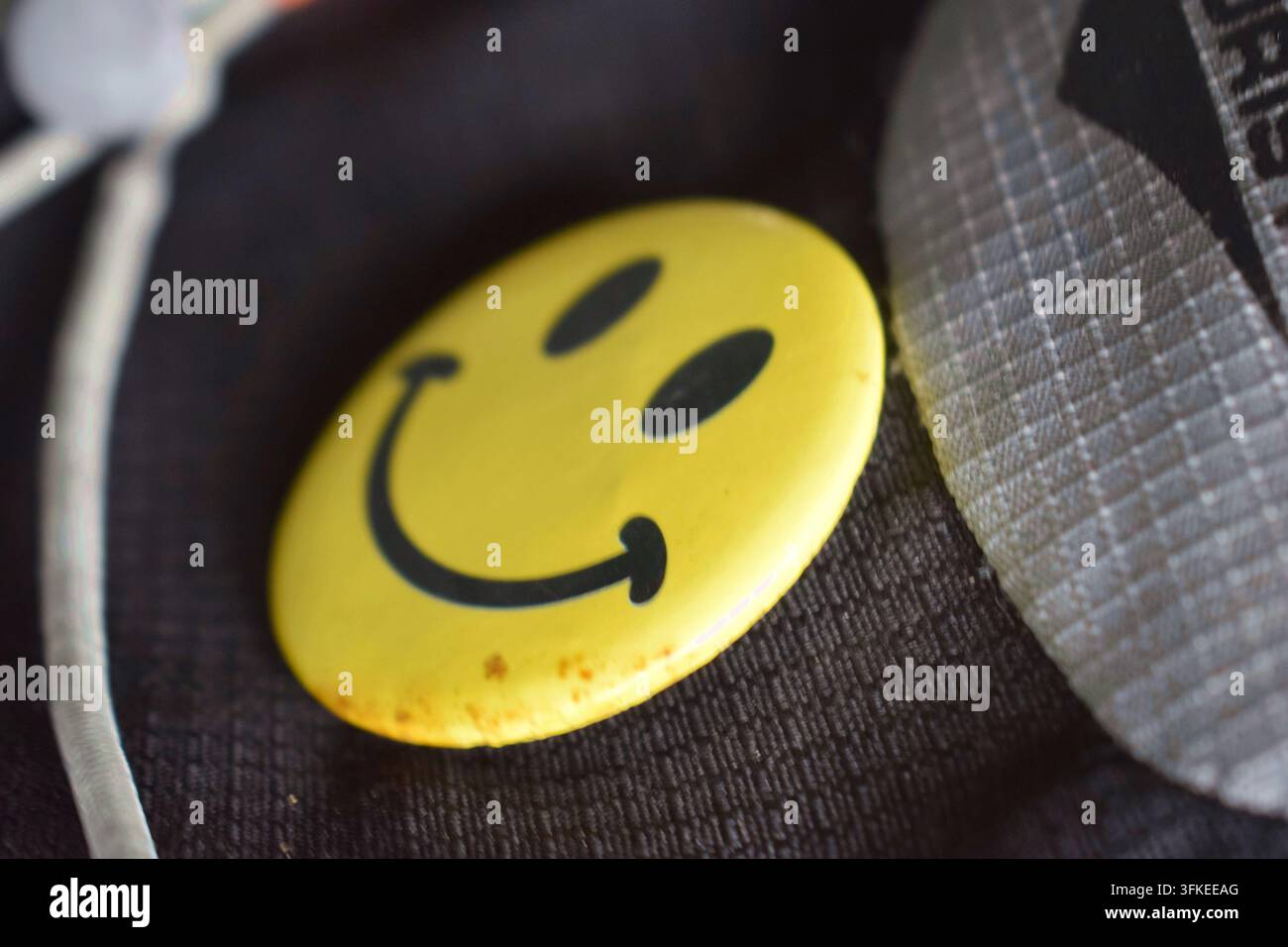 Gelbes Smiley-Gesichtsabzeichen, das auf dunklem Stoff ruht. Stockfoto