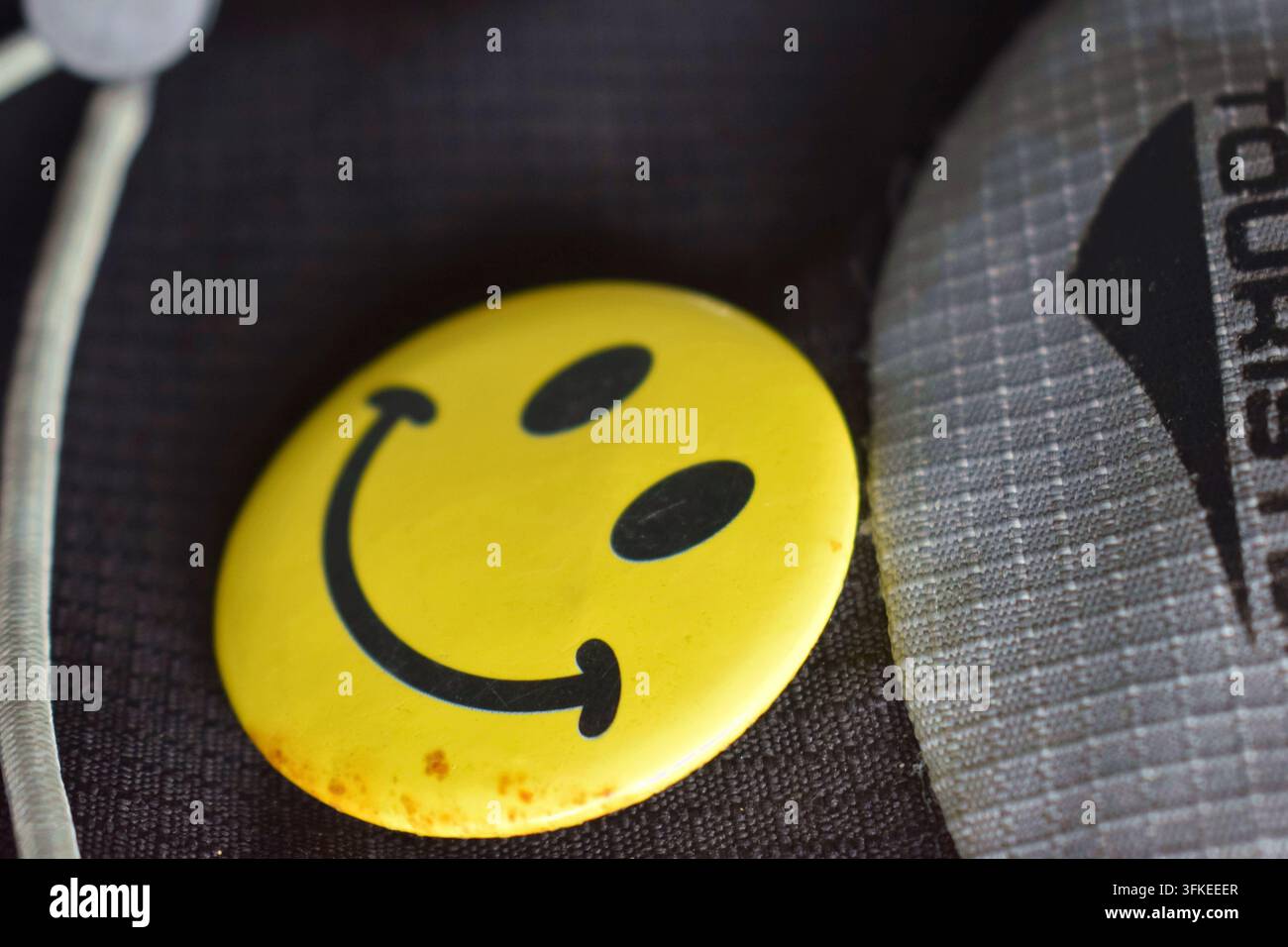 Gelbes Smiley-Gesichtsabzeichen, das auf dunklem Stoff ruht. Stockfoto