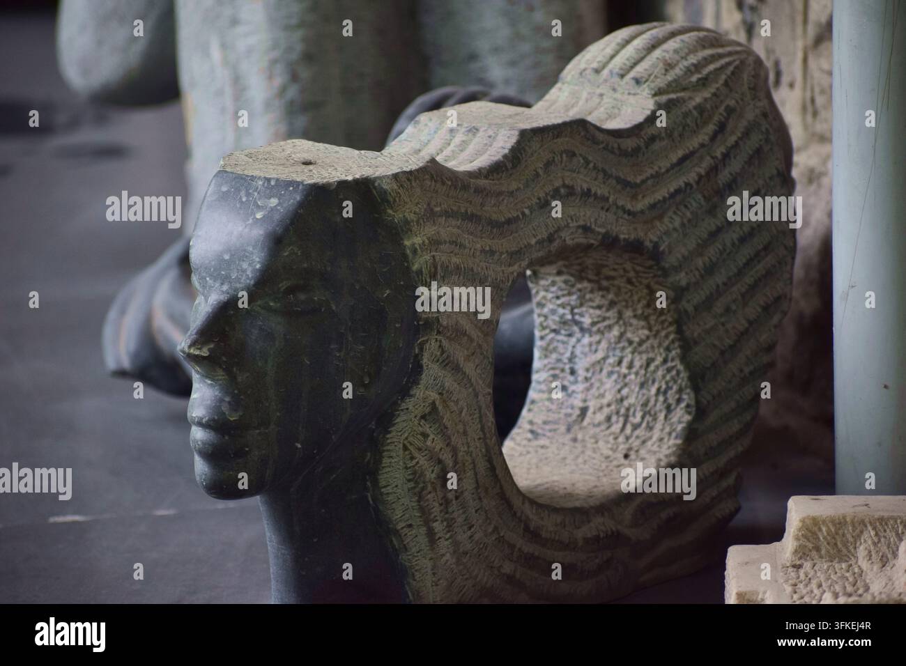 Verwitterte Steinskulptur eines menschlichen Gesichts, ausgestellt in einer Outdoor-Kunstausstellung. Stockfoto