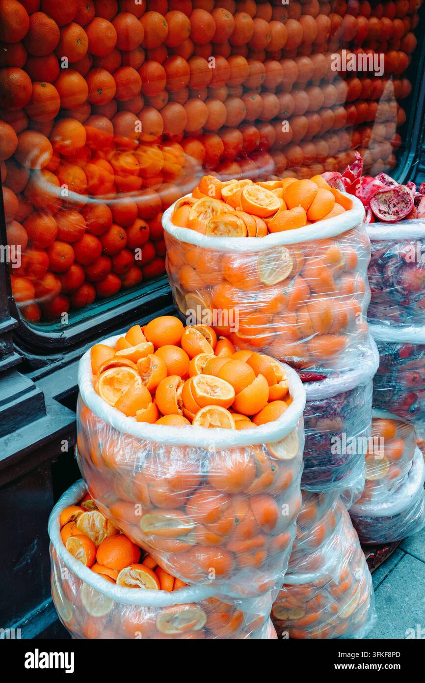 ausgepresste Orangenhälften füllen große Plastiktüten mit nach unten gerollten Rändern, neben Tüten mit weggeworfenen Granatapfelschalen und ganzen Orangen, die ausgestellt sind Stockfoto