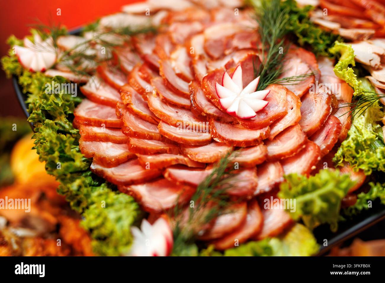 Ein ansprechendes Fleisch-Gastronomietablett mit kreisförmig angeordneten Scheiben geräuchertem Schinken, dekoriert mit frischem Salat und Rettichblüten. Stockfoto