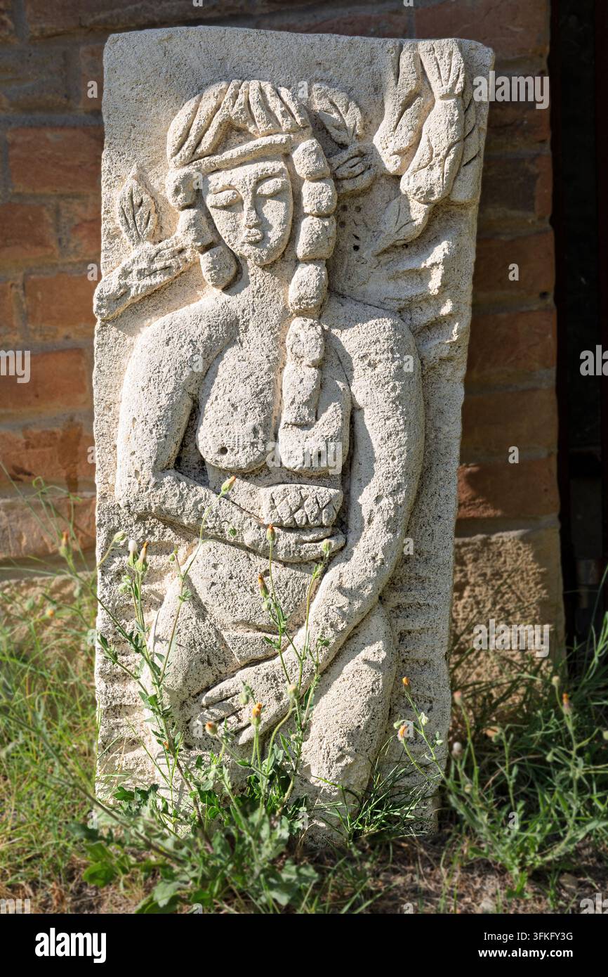 Geschnitztes Steinrelief einer weiblichen Figur, die möglicherweise eine Fruchtbarkeitsgöttin darstellt, die eine Weinflasche hält, Weingut, Dorf Rojljevac, Serbien Stockfoto