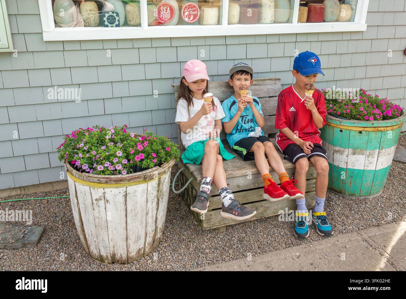 Lunenburg Halifax Nova Scotia Kanada,drei Kinder,asiatische Kinder,zwei Jungen,eine Tochter,Eis essen,Eiswaffeln,sitzende Kinder,Holzbank,Summe Stockfoto