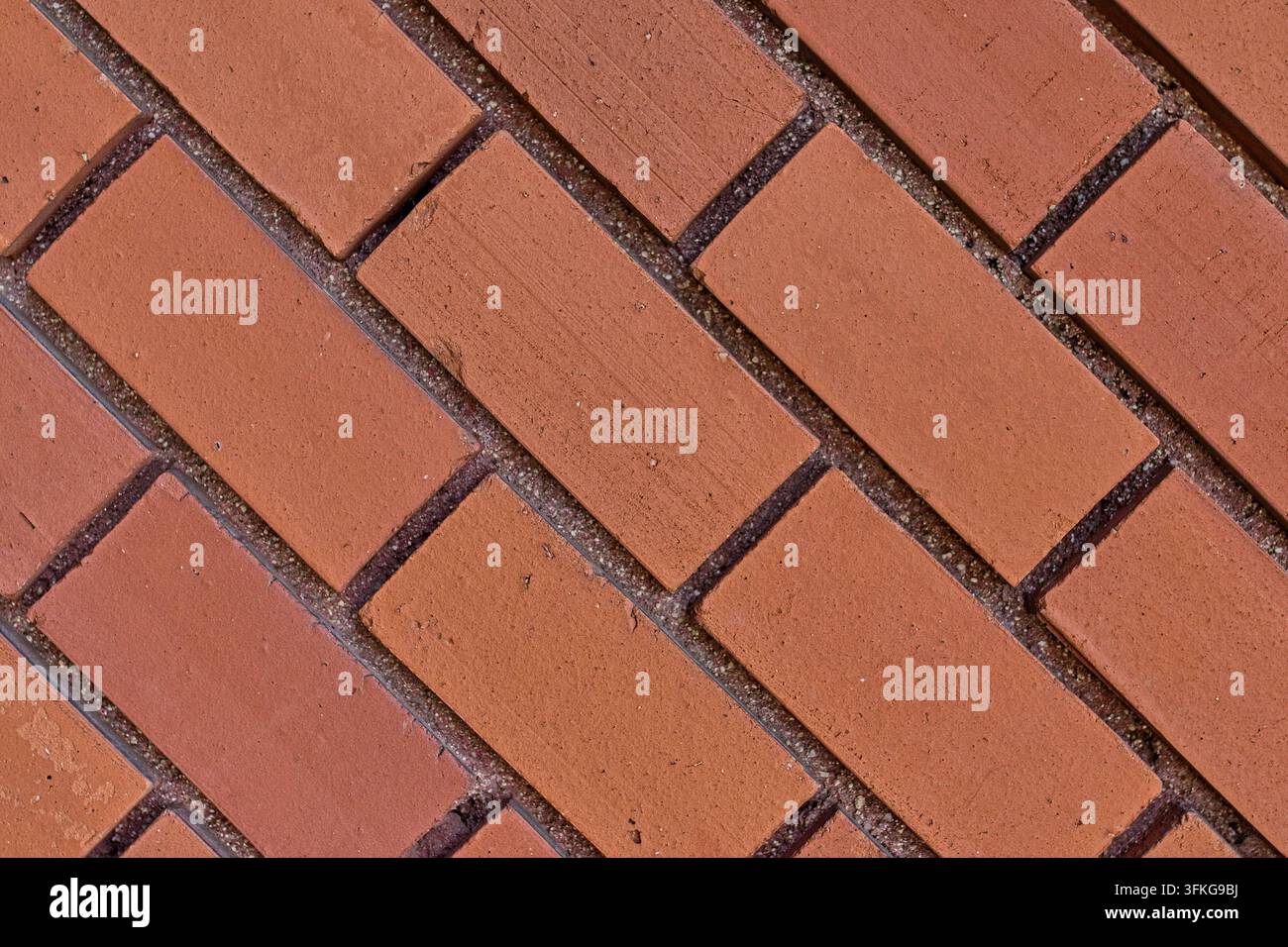 Nahaufnahme eines Fischgräten-Ziegelbelagmusters, diagonal verlegte orangefarbene Ziegel mit deutlichem Mörtel, Baumaterial und Gehweg. Stockfoto