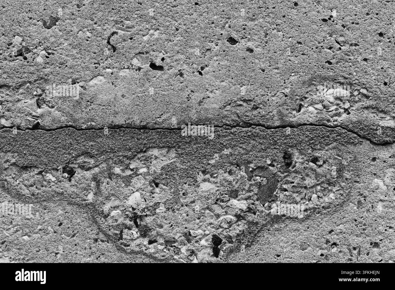 Nahaufnahme von rauem grauem Beton mit porigem Zuschlag, abgeplatzten Stellen und einem auffälligen horizontalen Riss, der eine gealterte Wandoberflächentextur bildet Stockfoto