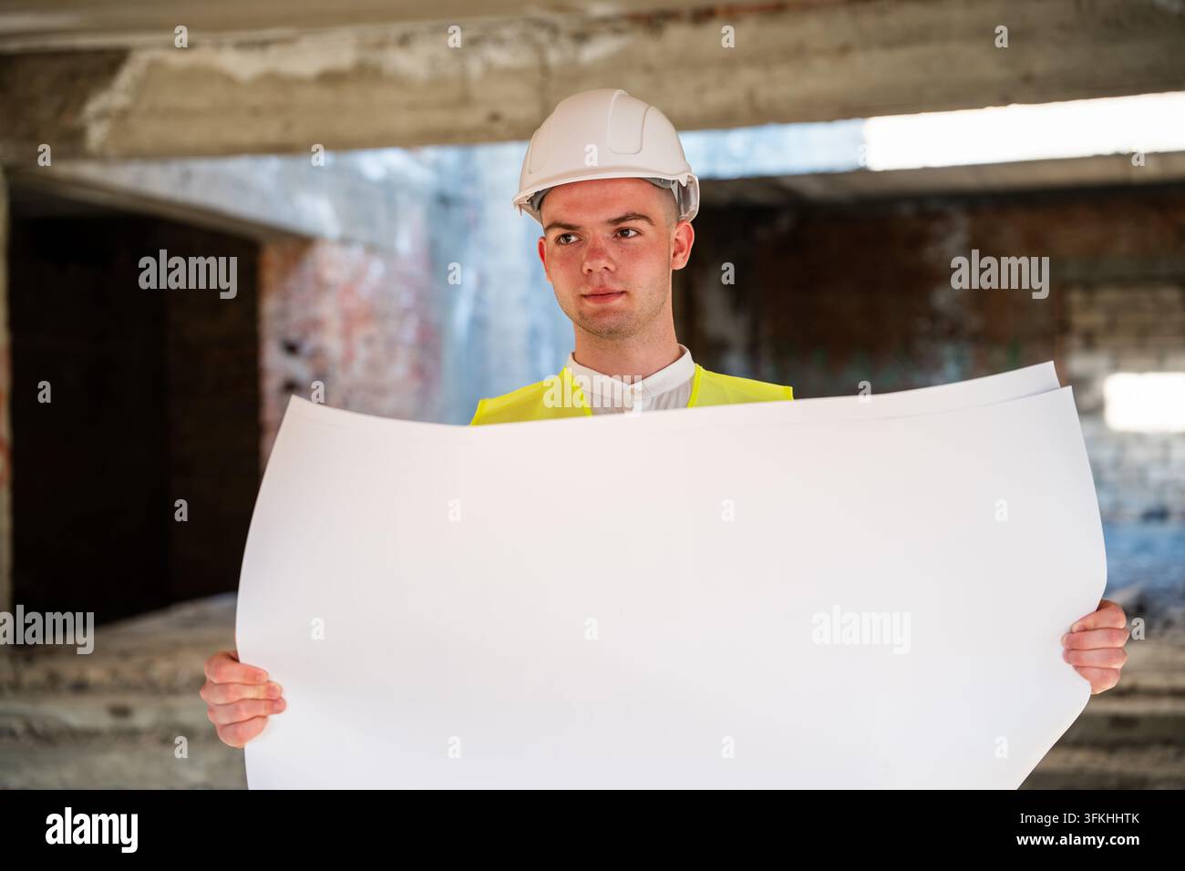 Bauprofi hält ein leeres Großformatblatt in einem unverputzten Gebäude. Renovierungsvorschlag und Projektvorlage für architektonische Dienstleistungen Stockfoto