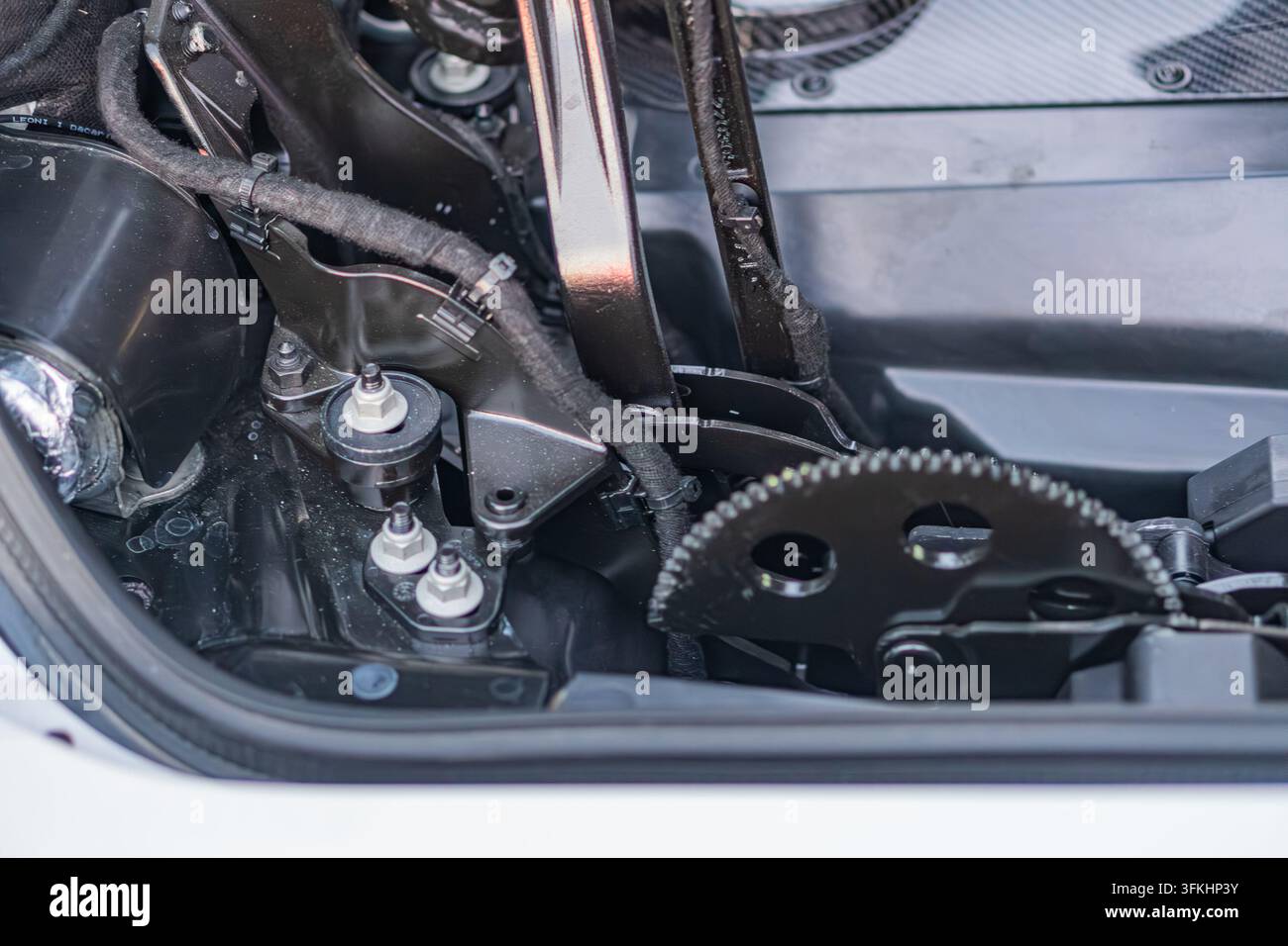 Nahaufnahme einer geöffneten Motorhaube eines Autos, die verschiedene Metall-, Elektro- und Flüssigkeitskomponenten unter hellem weißem Kunstlicht zeigt Stockfoto