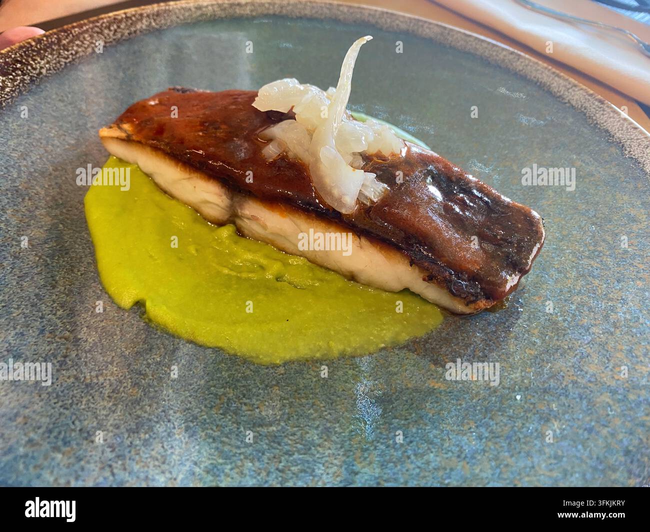 Gegrilltes Seebassfilet auf einem modernen Teller mit lebhaftem Erbsenpüree und eingelegtem Gemüse, angerichtet für feine Küche, elegante, frische Meeresfrüchtepräsentation für Stockfoto