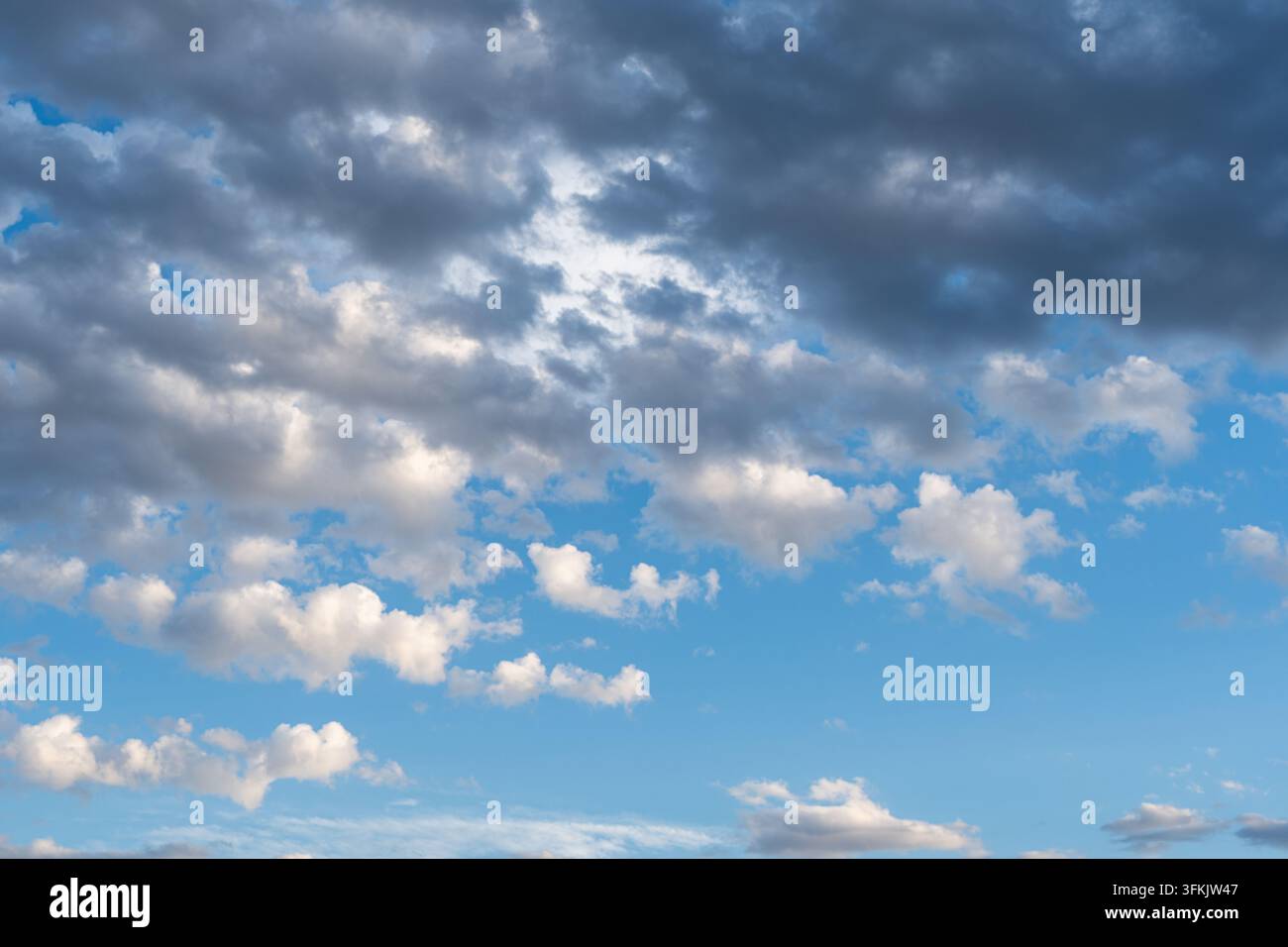Dunkle Gewitterwolken, die über dem blauen Himmel aufziehen, mit turbulenten weißen Wolken, die sich drehen Stockfoto