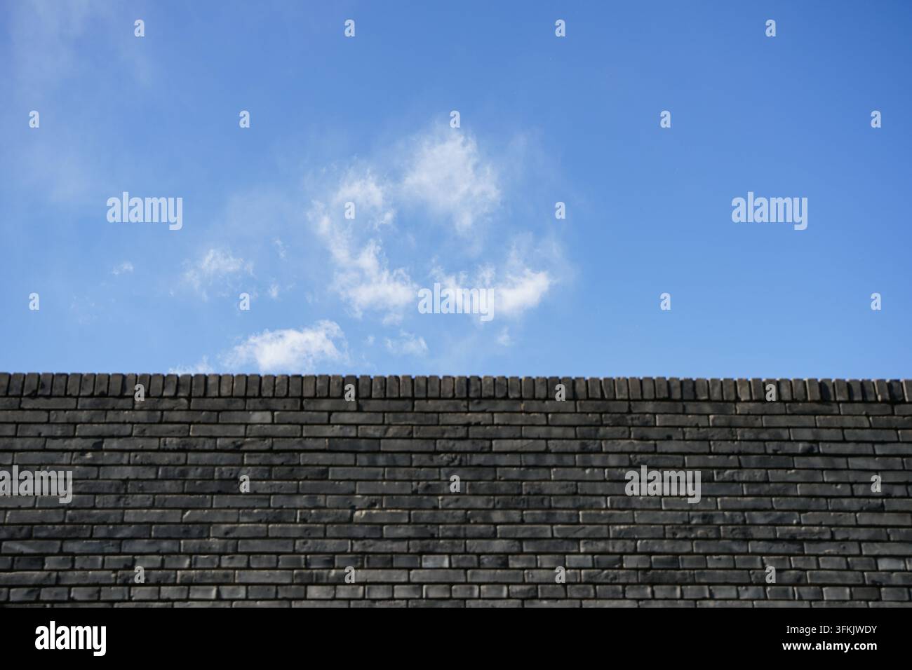 Schmaler Streifen blauen Himmels über einer verwitterten grauen Ziegelwand Stockfoto
