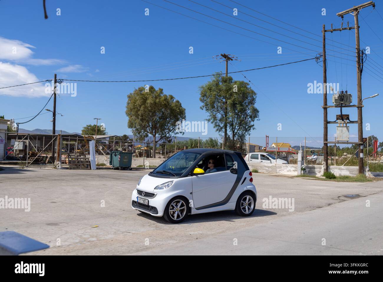 Zante, Griechenland, 9. September 2026: Straßenszene, die ein kompaktes Smart-Auto zeigt, das an Strommasten, Stromtransformatoren, Zäunen, Bäumen und Straßen vorbeifährt Stockfoto