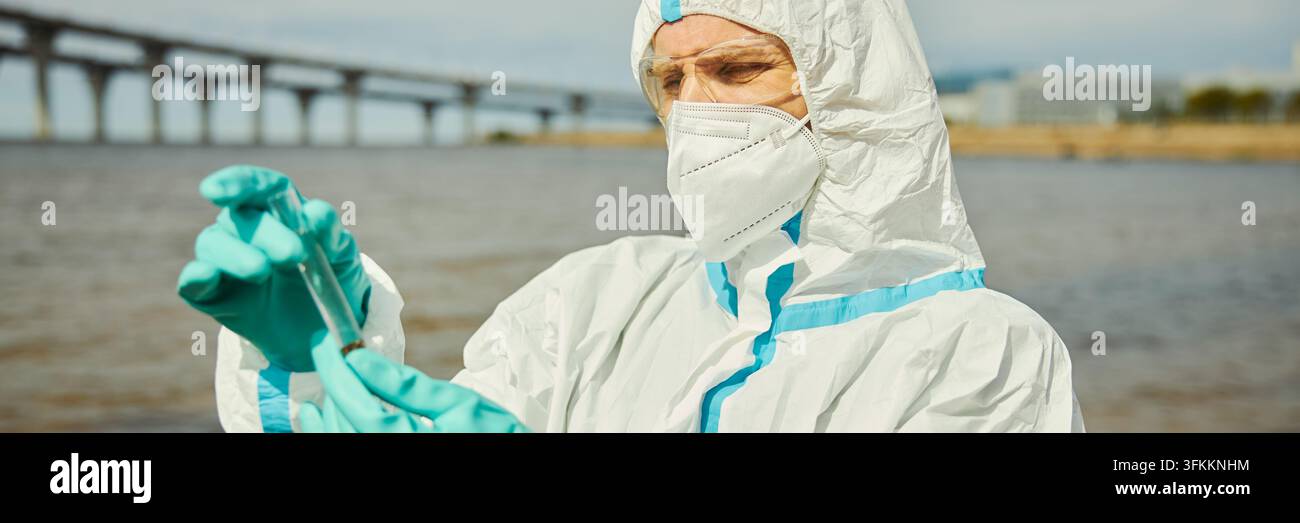 Kopf eines männlichen Wissenschaftlers in einem Schutzanzug, der eine Wasserprobe im Freien untersucht Stockfoto