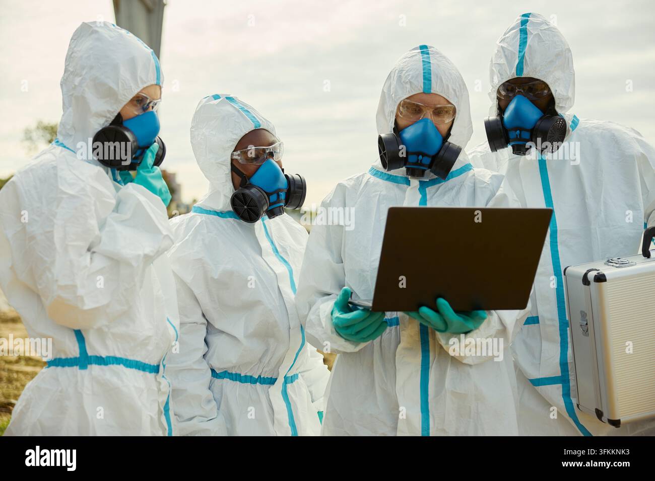 Verschiedene Wissenschaftler in Schutzanzügen, die Daten auf einem Laptop im Freien analysieren Stockfoto