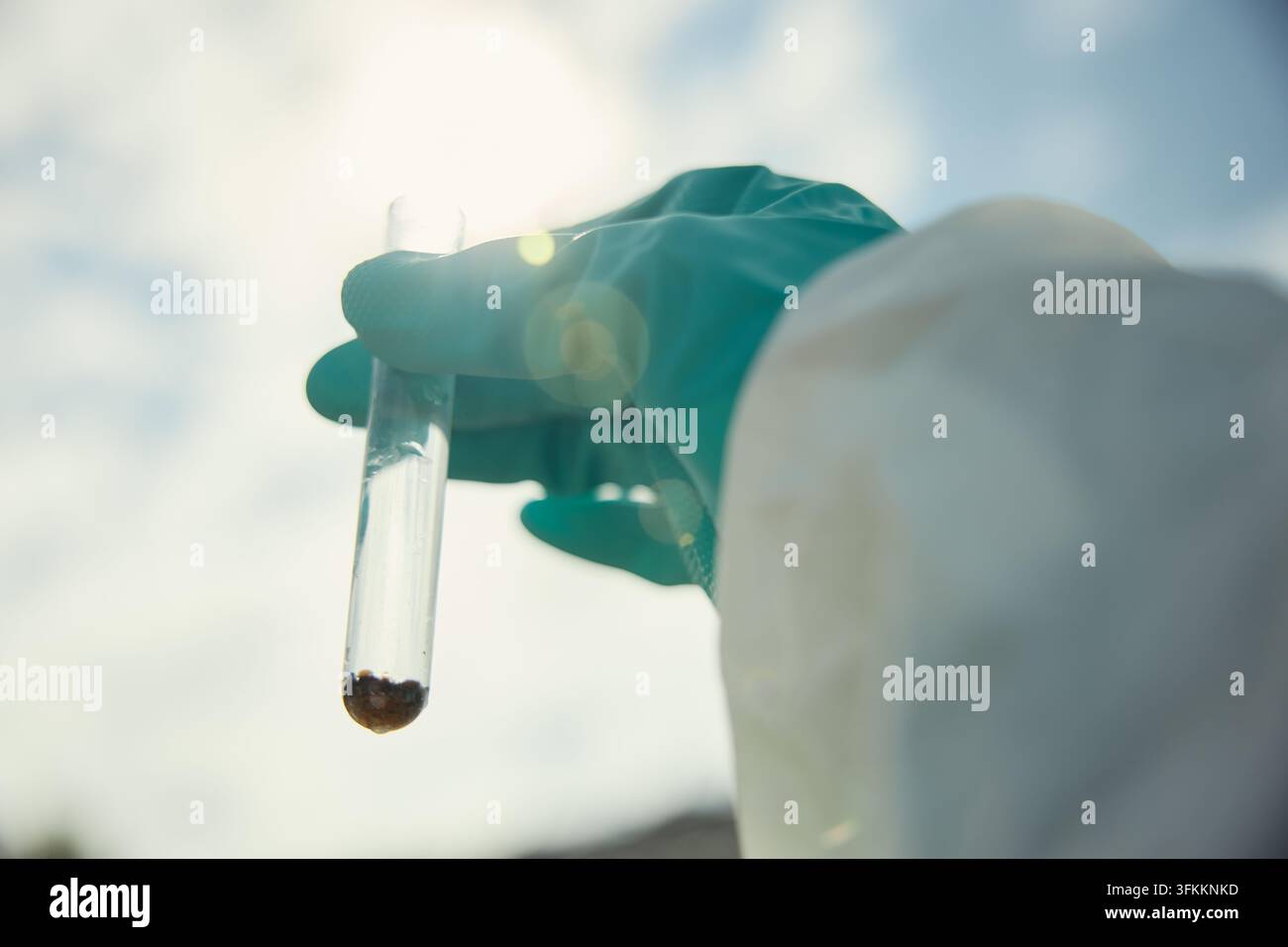 Wissenschaftler in Schutzanzug hält ein Reagenzglas mit Bodenprobe Stockfoto