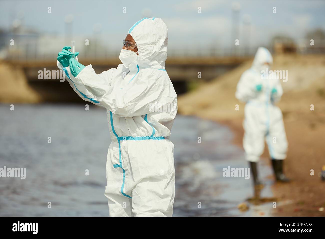 Schwarze Frau, Ökologin im Schutzanzug, untersucht Wasserprobe im Freien Stockfoto