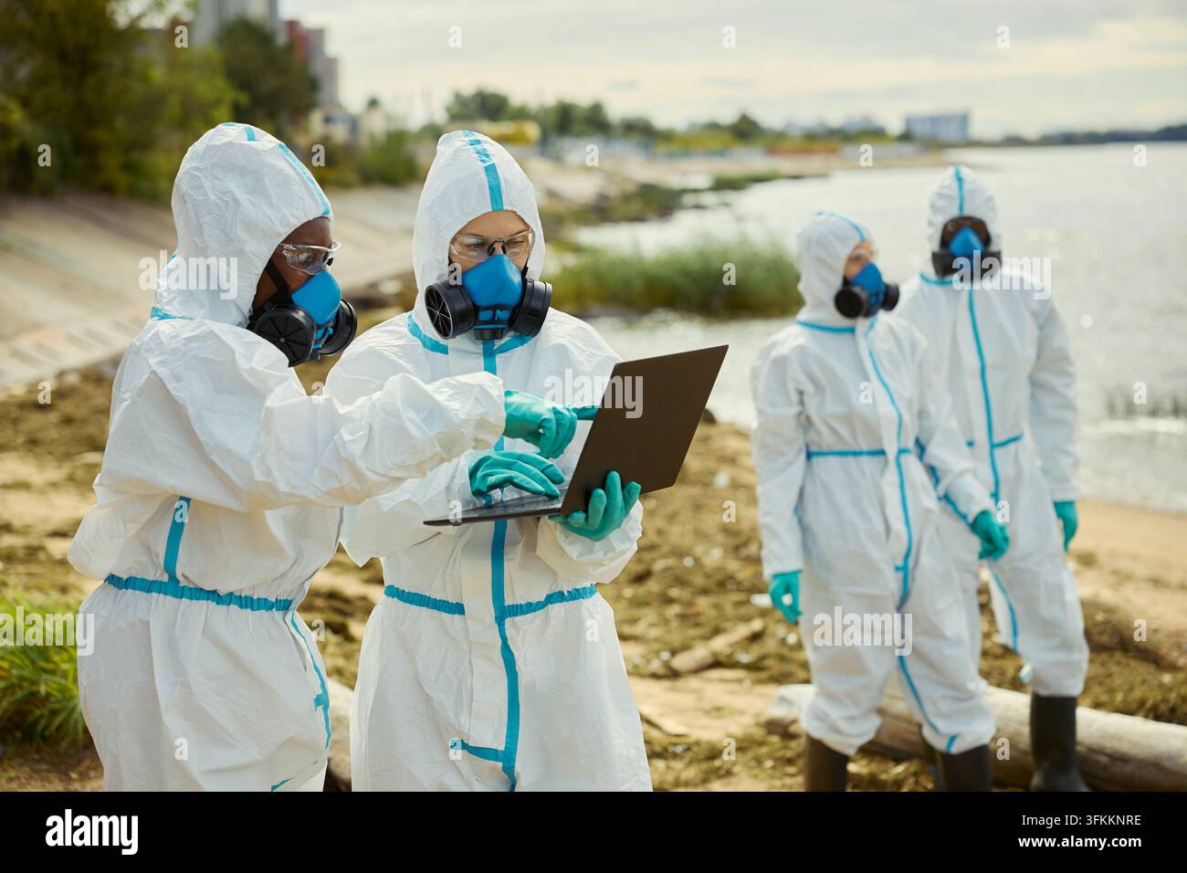 Ökologen in Schutzanzügen, die während der Wasserforschung im Freien einen Laptop benutzen Stockfoto