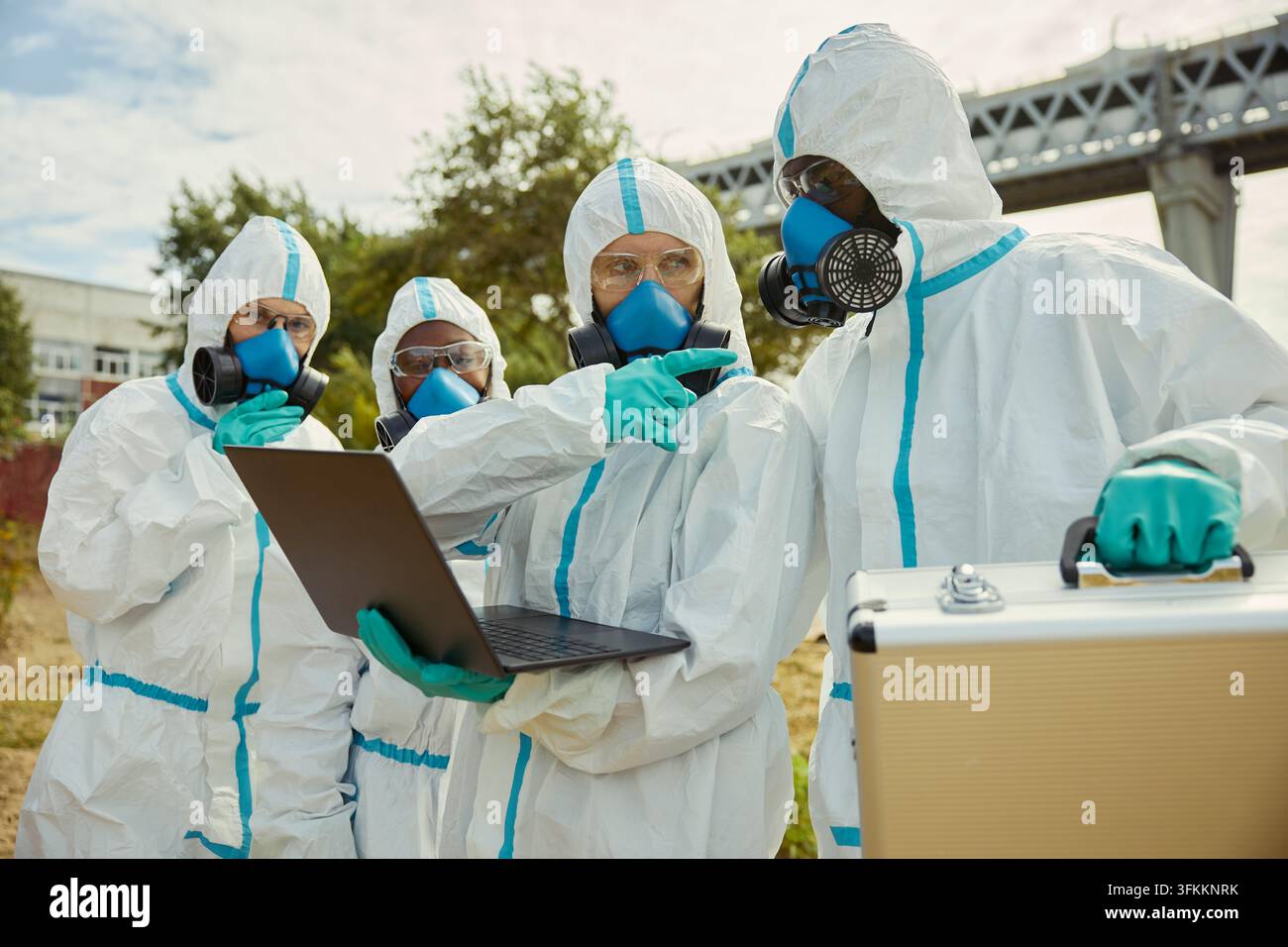 Verschiedene Wissenschaftler in Schutzanzügen, die im Freien mit einem Laptop arbeiten Stockfoto