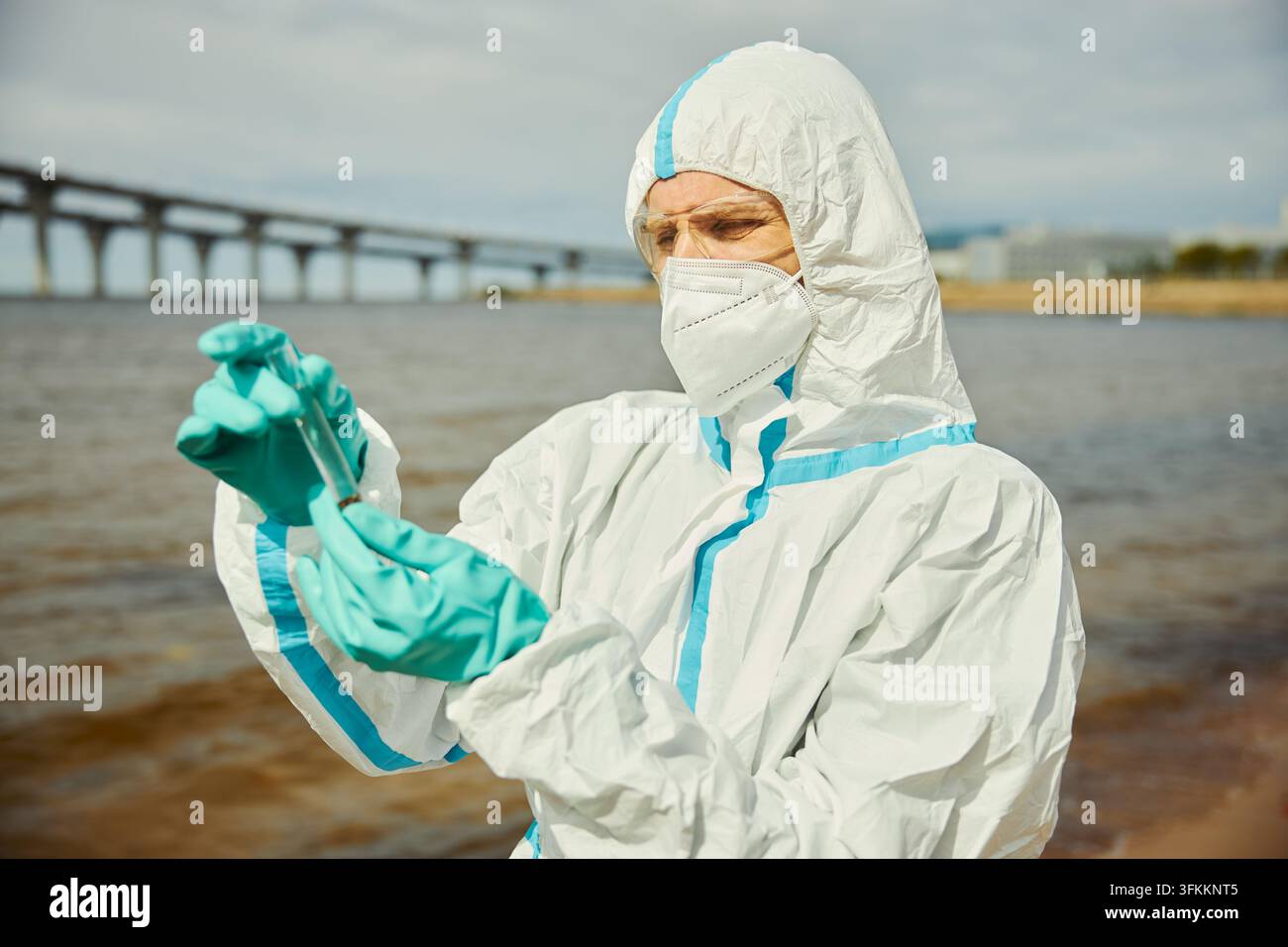 Wissenschaftler in Schutzanzug untersucht Wasserprobe im Freien Stockfoto