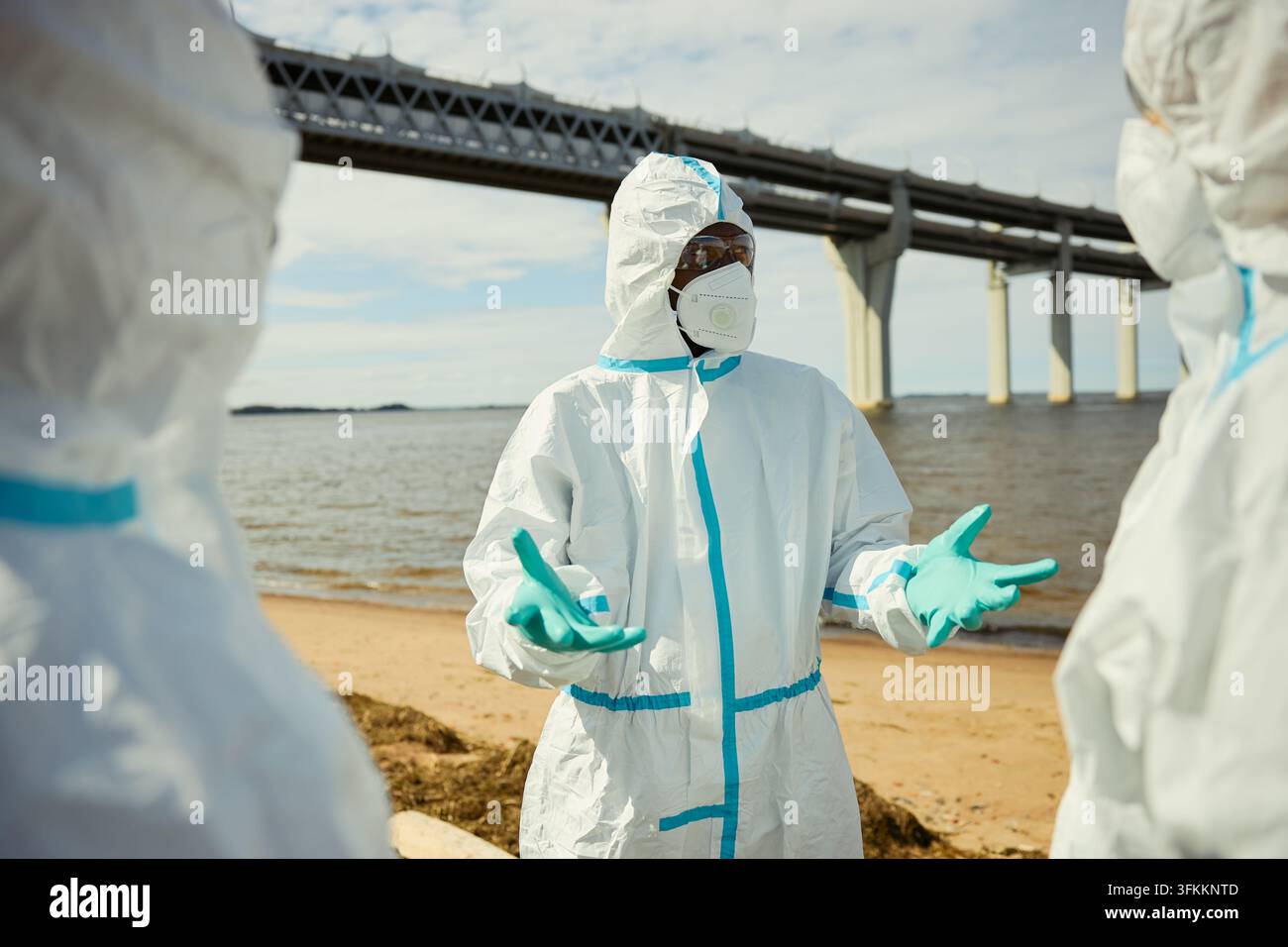 Schwarzer männlicher Wissenschaftler in einem Schutzanzug, der im Freien mit einem Team spricht Stockfoto