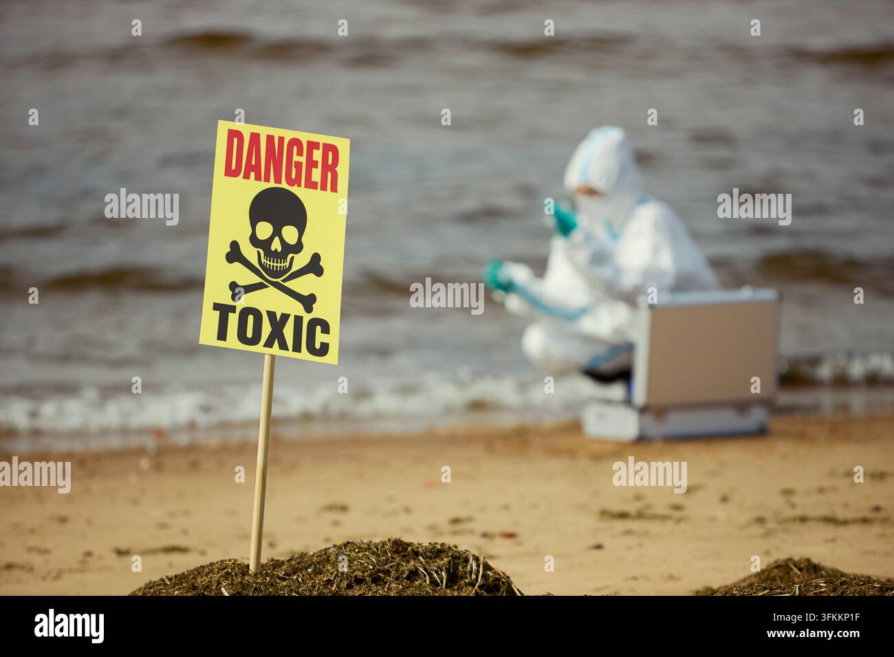 Giftgefahr-Schild an der Küste mit Wissenschaftler, der Wasser untersucht Stockfoto