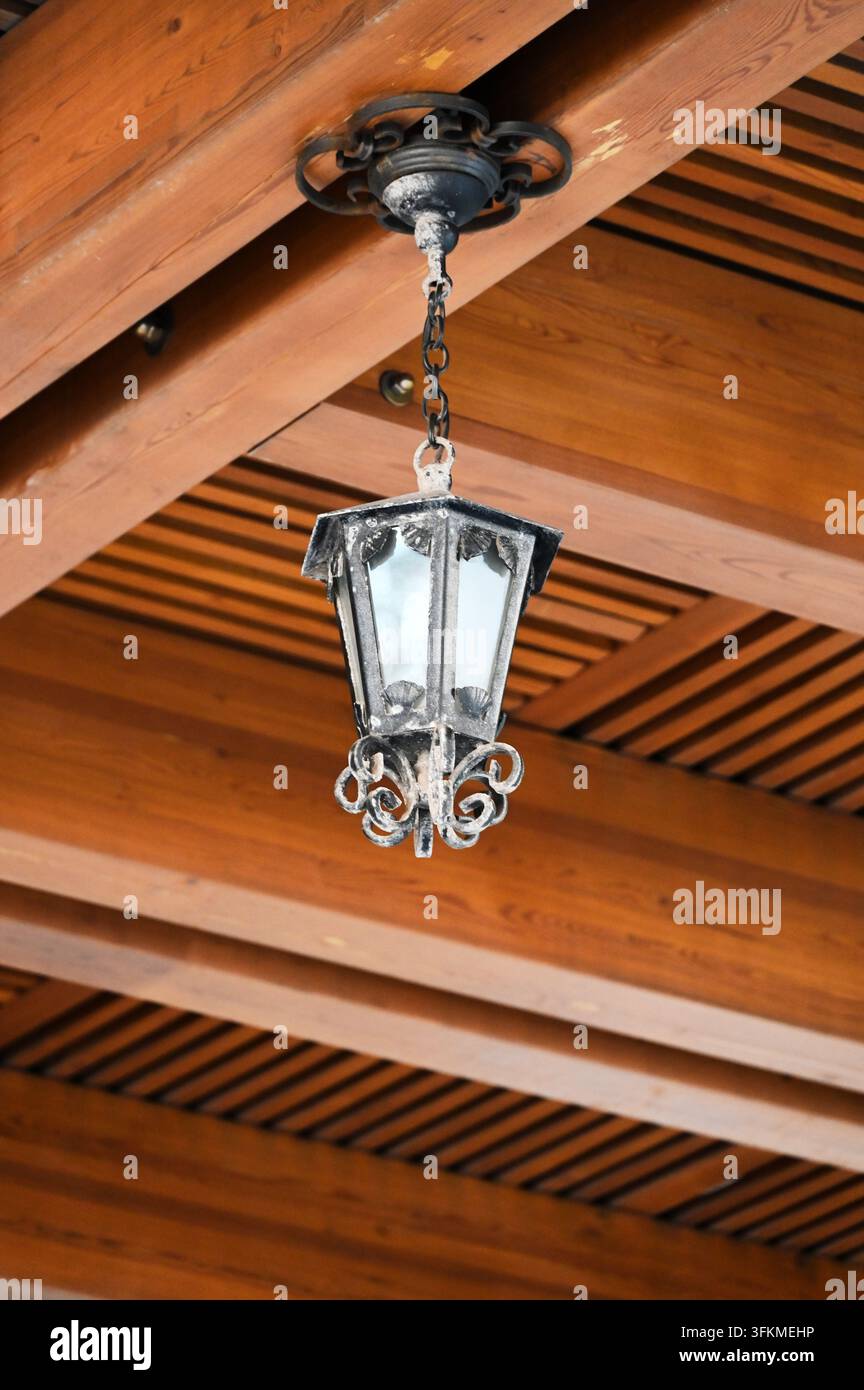 Vertikale detaillierte Fotografie einer antiken schwarzen Metall-Hängelampe, die an einem rustikalen Holzbalken-Deckenbalken montiert ist Stockfoto