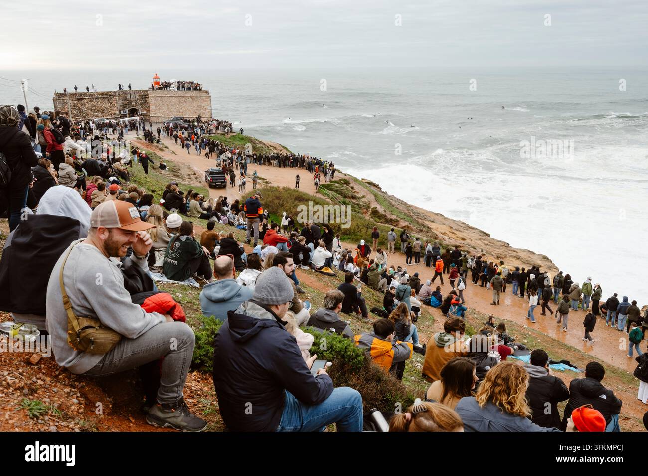 Nazare, Portugal - 6. Dezember 2025: Menschen stehen auf Klippen und beobachten den Ozean und die großen Wellen bei Sonnenuntergang in Nazare, Portugal Stockfoto