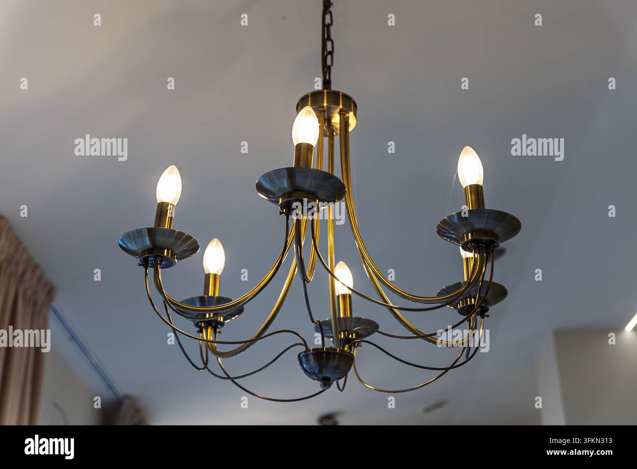 Eleganter Messing-Kronleuchter mit blauen Glasakzenten und warmen Lichtern Stockfoto