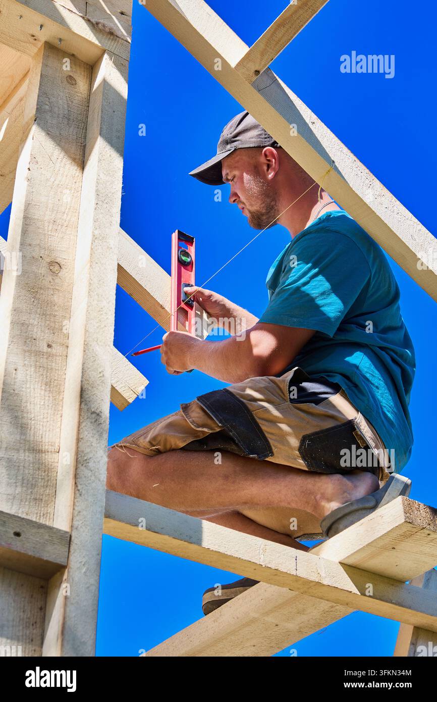 Holzgerüst aus dem Stegreif hält den Zimmermann, während er mit einem Taschenlot einen Dachbinder ausrichtet, während er das Gerüst baut. Stockfoto