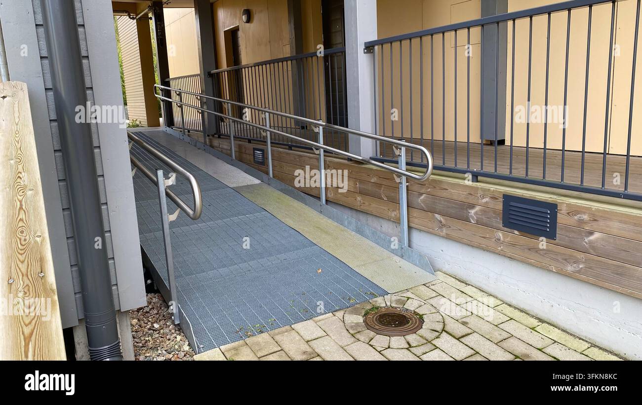 Zugängliche Rollstuhlrampe mit Metallgeländern am Eingang eines Wohngebäudes Stockfoto