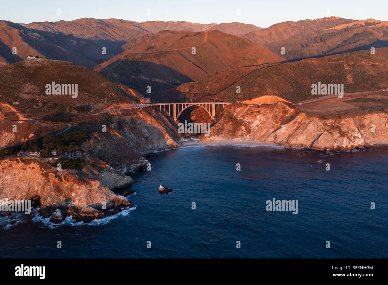 Luftbild zeigt die Bixby-Creek-Brücke, die vom Sonnenlicht des Sonnenuntergangs beleuchtet wird, entlang der Highway 1 in Big Sur, Kalifornien, die sich über ein raues Canyon neben dem Pazifik erstreckt Stockfoto