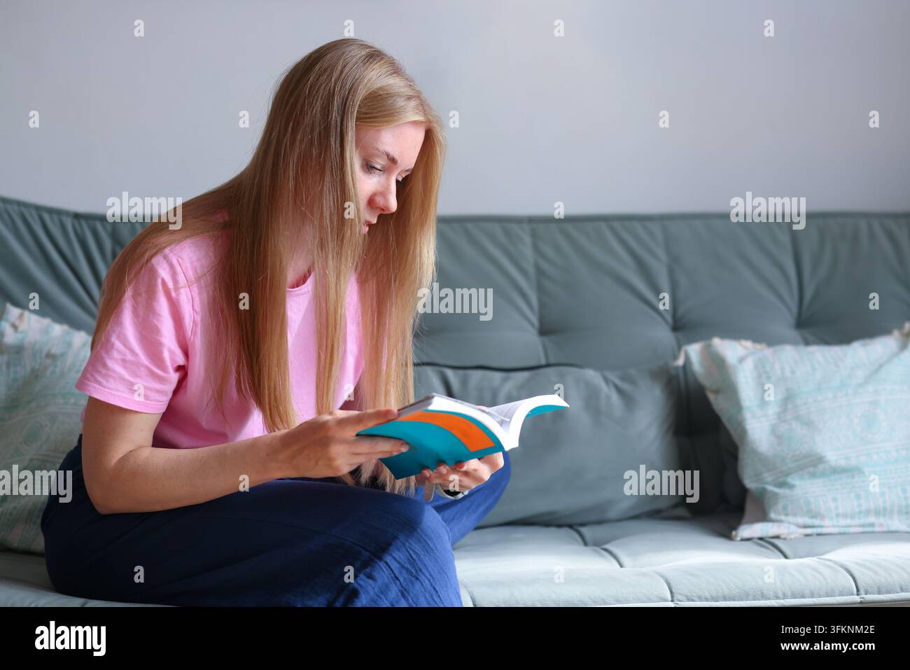 Frau entspannt sich auf einem Sofa mit Papierbüchern und fördert das Lesen als achtsame Freizeitbeschäftigung, digitale Entgiftung und Stressabbau. Stockfoto