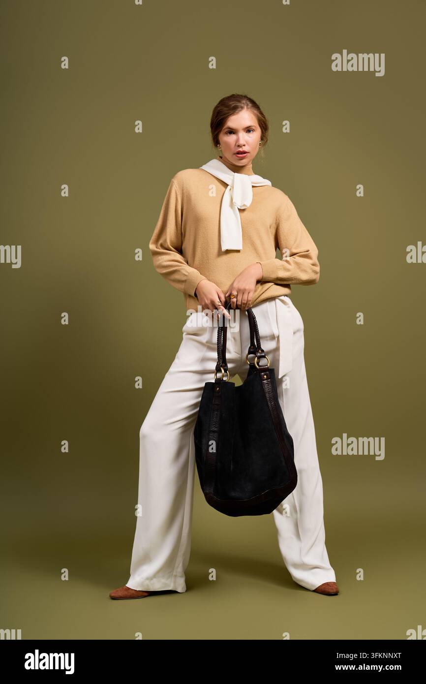Gemütliche Herbstästhetik erwacht zum Leben, während eine Frau ein stilvolles Herbstoutfit und eine Handtasche präsentiert Stockfoto